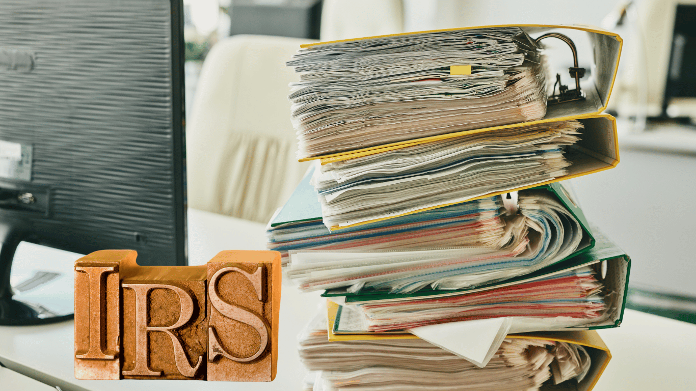 Wooden blocks spelling out IRS next to as stack of paperwork on a desk